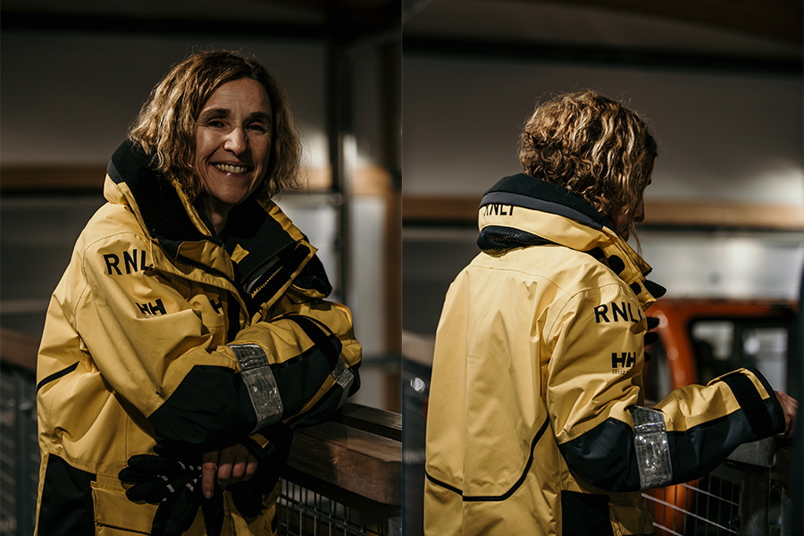 Smiling crew member in a yellow and navy RNLI offshore jacket, seen from the front and behind