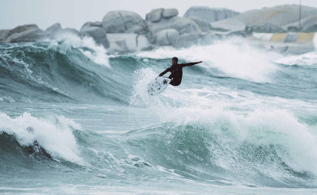 Surfer in a hooded winter wetsuit walking into cold water