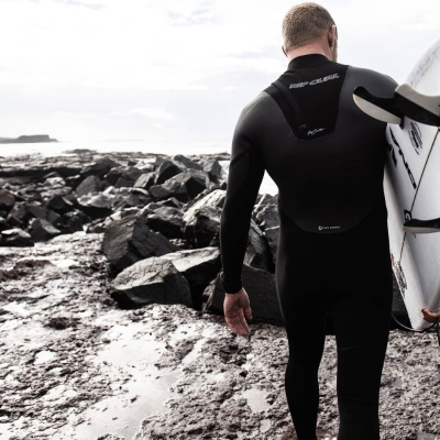 Surfer i våddragt tager en handske på ved havet