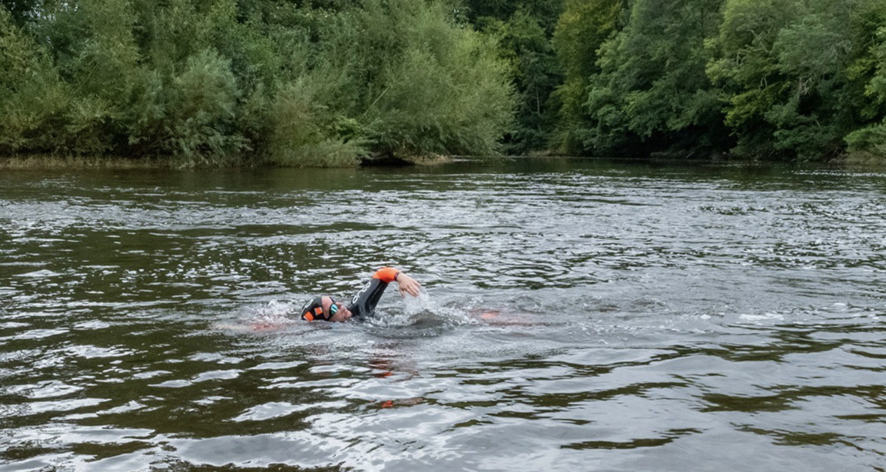 Swimmer doing front crawl in a wide tree-lined river, towing a small orange float