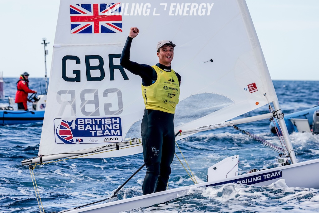 Sailor in a yellow leader's bib punching the air in celebration aboard his GBR dinghy at sea