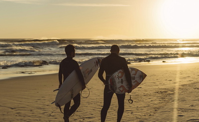 Surfers in wetsuits silhouetted against a sunset