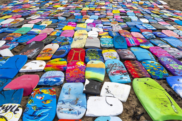 Dozens of brightly coloured bodyboards laid out in rows on a stone surface