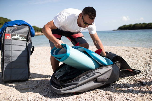 Man on a beach putting a deflated SUP board into a storage bag